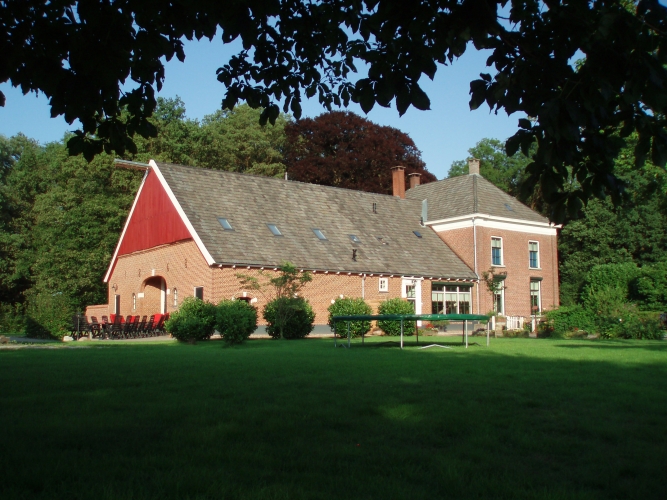 De boerderij van Landgoed Wissink met rood pannendak tussen de bomen, gezien vanaf het grasveld